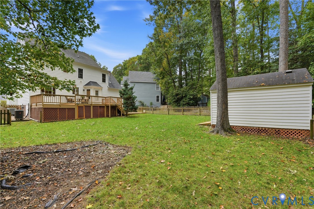 Backyard featuring a raised wooden deck, lattice skirting, detached storage structure, and perimeter wood fencing surrounded by mature trees