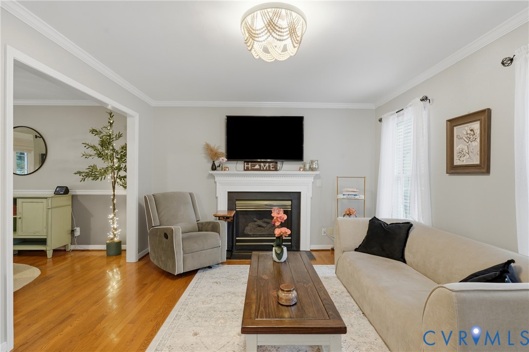 Living area featuring a fireplace with a white mantel, wood-finish flooring, crown molding, and a tiered beaded flush-mount light fixture