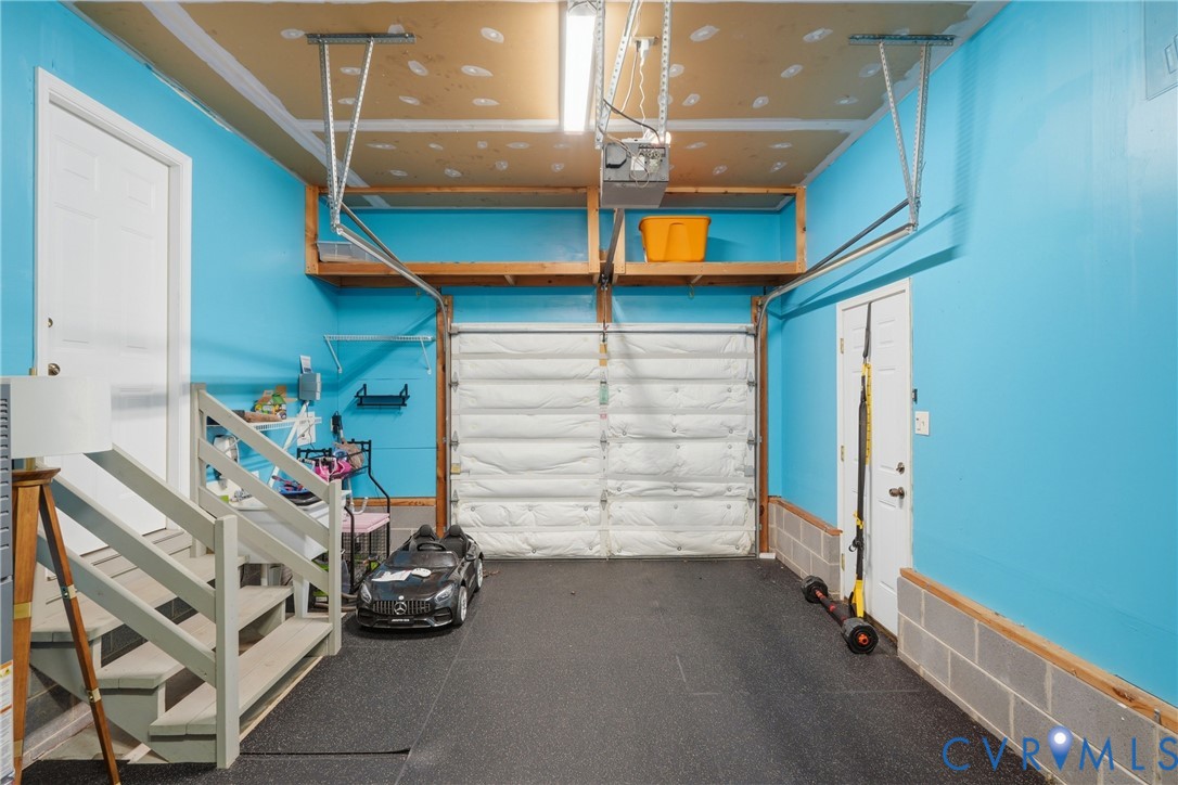 Garage featuring an insulated sectional door, overhead wood-frame storage shelving, dark textured flooring, and interior wooden staircase