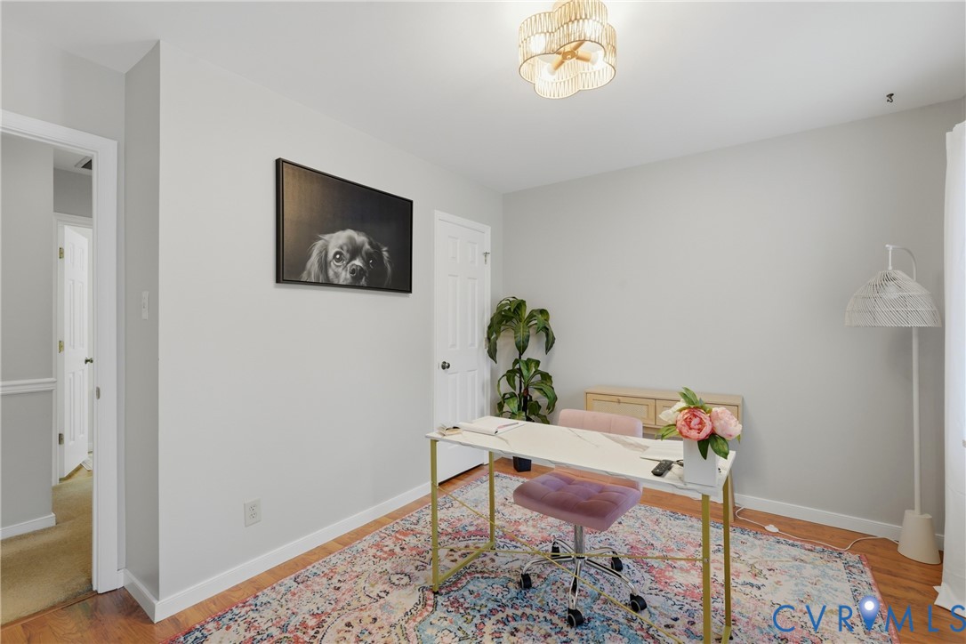 Interior room featuring wood-finish flooring, a neutral wall color palette, a six-panel door, and a multi-tiered decorative ceiling light fixture
