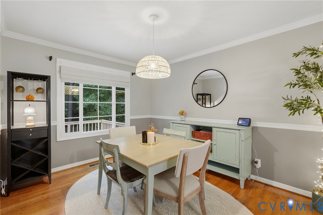 Room featuring wood-finish flooring, crown molding, chair rail trim, and a woven pendant light fixture