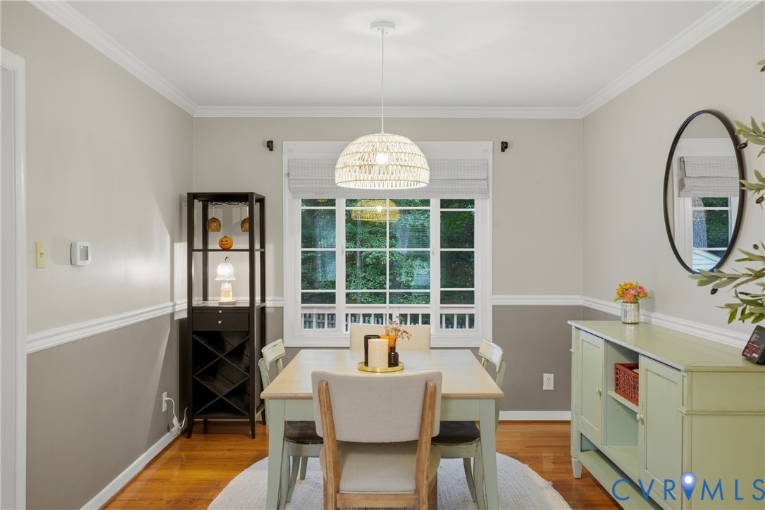 Dining space featuring wood-finish flooring, white crown molding, crisp chair rail, multi-pane window with custom blinds, and a central dome pendant light fixture