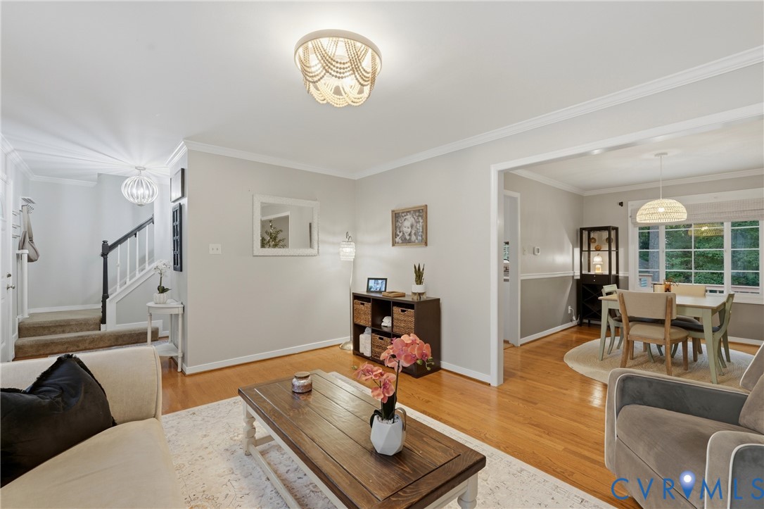 Hardwood flooring, crown molding, multi-tiered bead-embellished semi-flush mount lighting, and staircase with a stained wood handrail