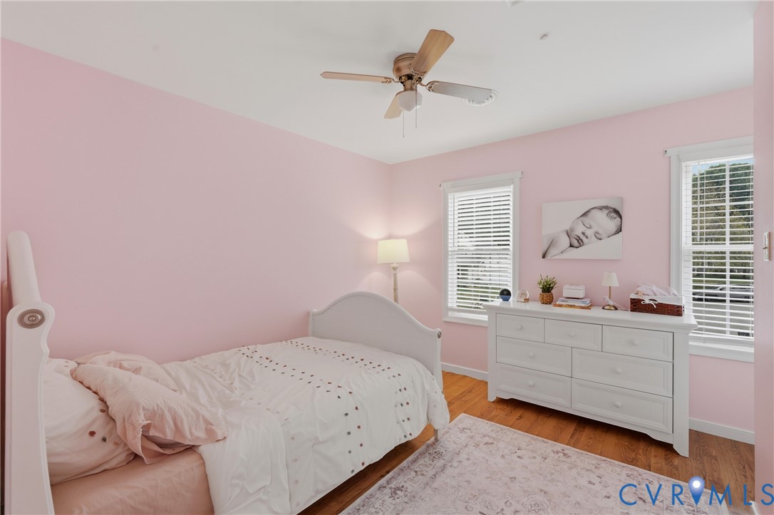 Room featuring wood-finish flooring, two windows with horizontal blinds, and a central ceiling fan with integrated lighting