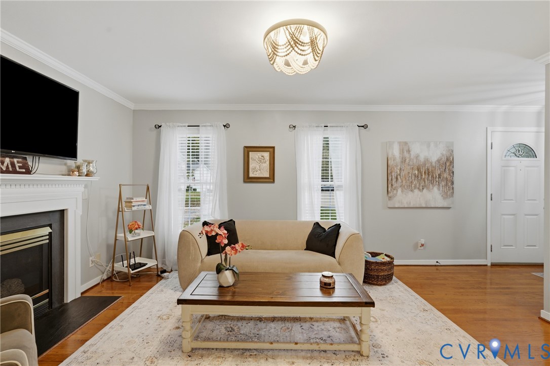 Living area featuring wood-finish flooring, a fireplace with a decorative mantel, crown molding, and a beaded semi-flush mount light fixture