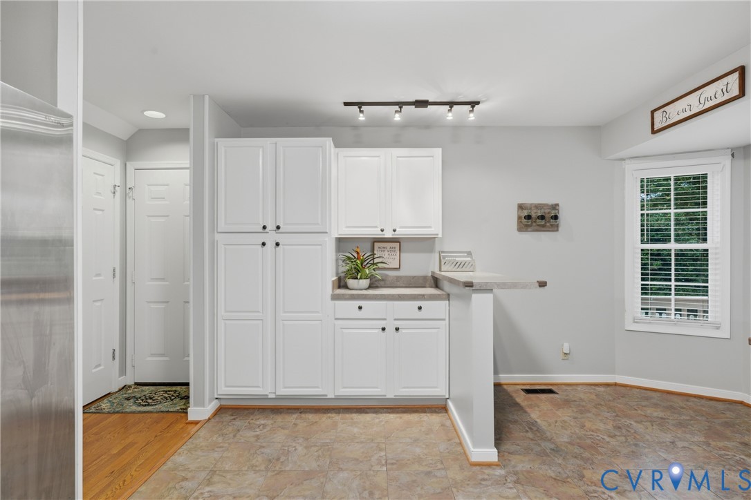 White cabinetry with ample storage, stone-finish countertops, multi-directional track lighting, and a multi-pane window