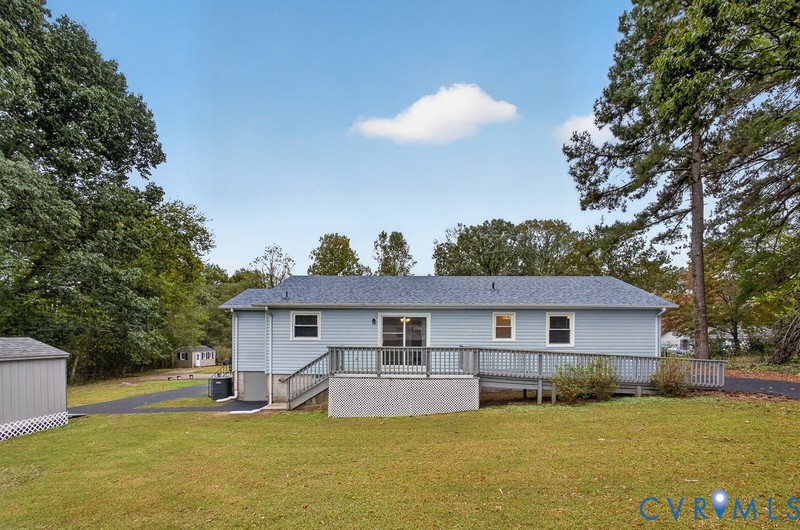 Exterior featuring light blue horizontal siding, shingled roof, attached elevated wooden deck with railings, and an asphalt driveway