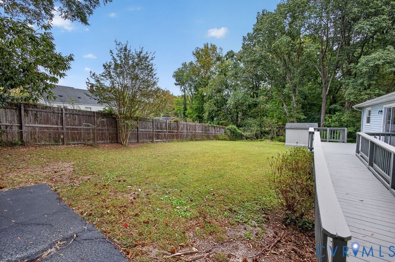 Expansive backyard featuring a leveled grass lawn, wood privacy fencing, a raised deck with railings, and a detached storage shed