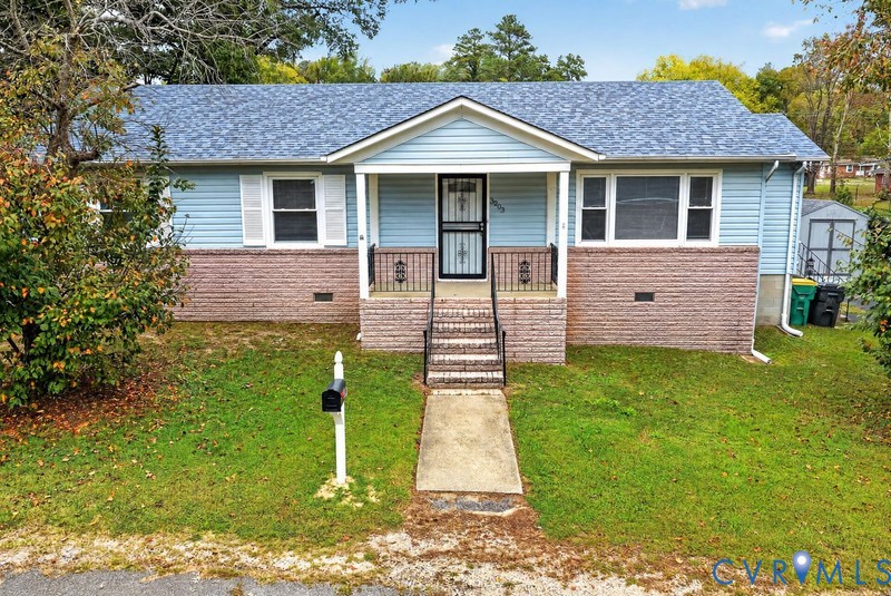 Single-story residence featuring blue horizontal siding, brick facade accents, a front porch with decorative iron railings, and architectural shingle roofing