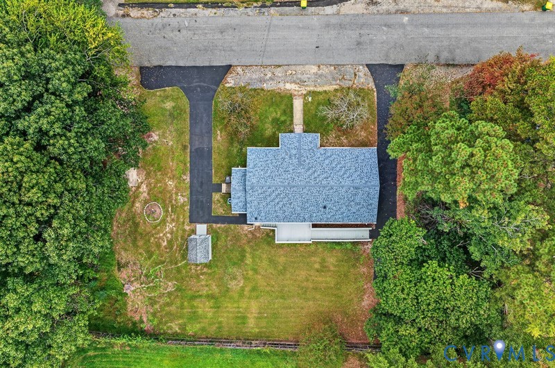 Aerial perspective of property featuring an expansive lawn, dual asphalt driveways, a detached storage structure, and extensive mature tree coverage