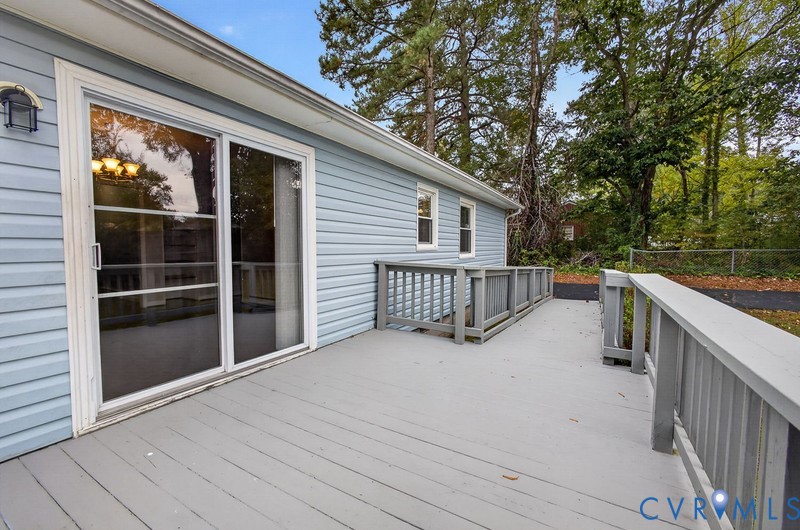 Exterior wood-finish deck with painted railings, horizontal lap siding, and sliding glass door