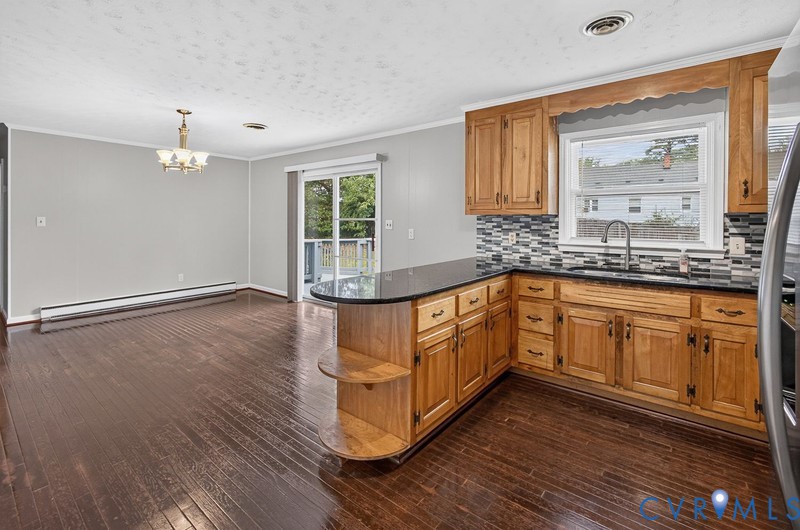Kitchen featuring wood cabinetry, stone countertops, multi-tonal tile backsplash, wood-finish flooring, and sliding glass doors