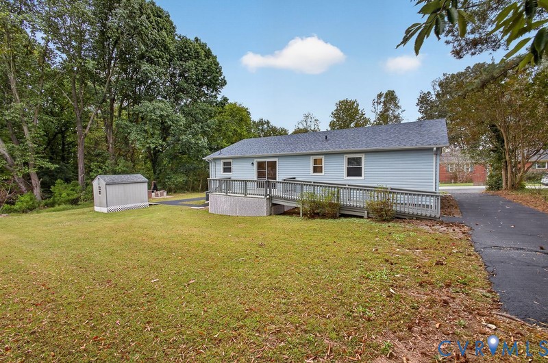 Exterior of the residence featuring horizontal siding, asphalt shingle roofing, an elevated wood deck with a ramp, a detached storage structure, and paved driveway