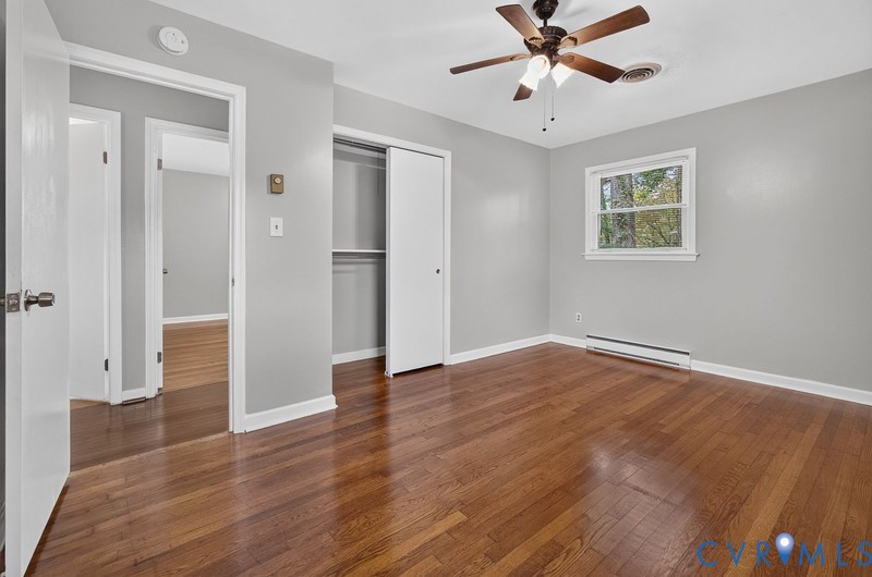 Wood-finish flooring, neutral wall paint, multi-light ceiling fan, and built-in closet with sliding doors