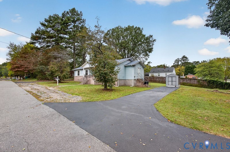 Single-story residence featuring vinyl siding, a front porch with metal railings, a paved driveway, and an exterior storage structure