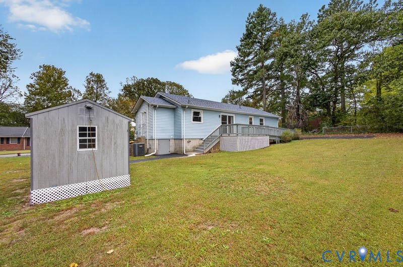 Light blue siding exterior featuring a multi-level wood deck, detached storage shed with lattice skirting, and a spacious lawn with mature trees