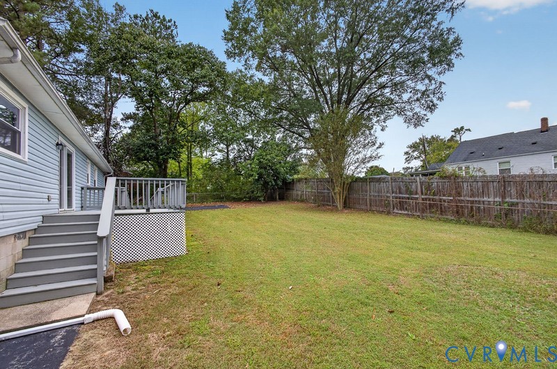 Rear yard featuring a raised wooden deck with staircase, horizontal wood fencing, and mature trees