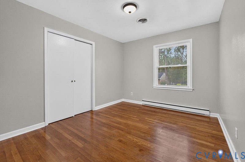 Neutral-toned interior room featuring wood-finish flooring, a double-door closet, and a single-pane window with white trim