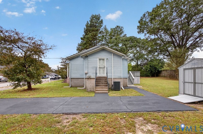 Light blue vinyl-sided exterior featuring a concrete foundation, asphalt driveway, detached storage shed, and rear wooden deck