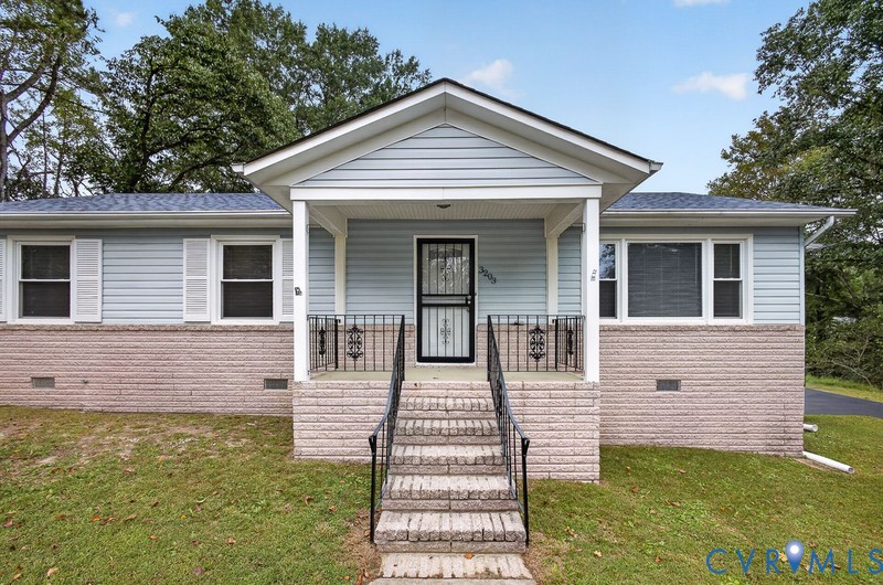 Exterior featuring light blue horizontal siding, a masonry lower facade, a covered front porch with iron railings, and a shingled gable roof