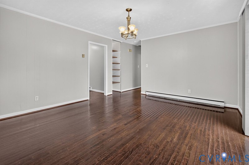 Interior space featuring dark wood-finish flooring, a multi-arm metallic chandelier, neutral wall tones, and open built-in shelving