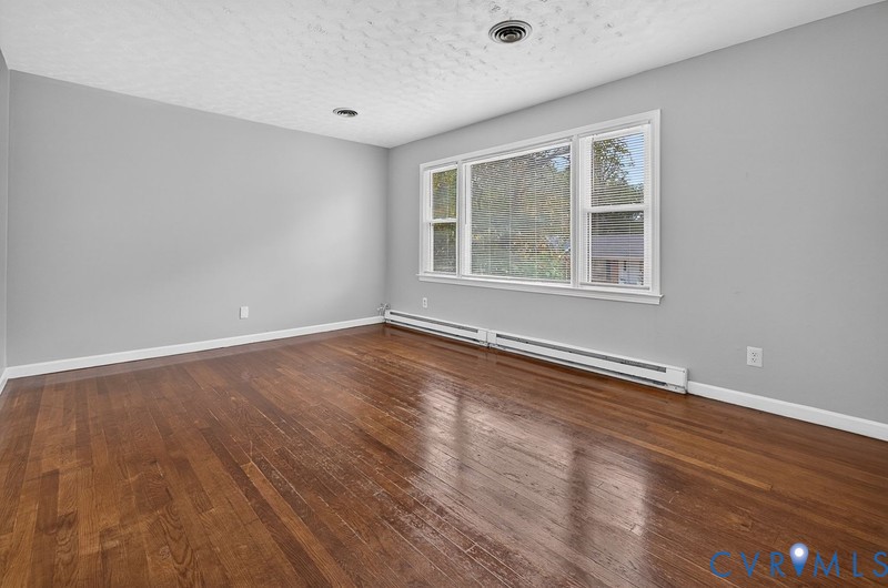 Spacious room featuring wood-finish flooring, large multi-pane windows, and neutral wall tones
