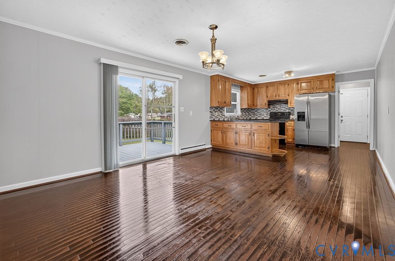 Open-concept interior featuring wood-finish flooring, oak cabinetry, stainless steel refrigerator, mosaic tile backsplash, and sliding glass doors