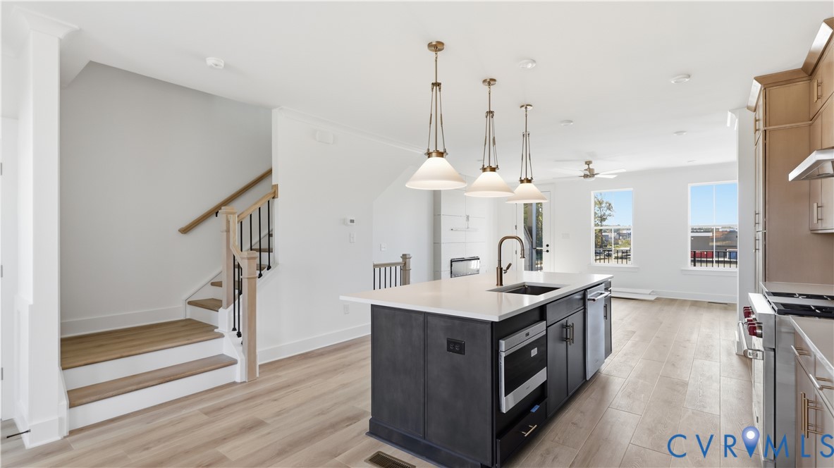 Kitchen featuring a center island with quartz countertops, custom dark cabinetry, stainless steel appliances, pendant lighting, and wood-finish flooring