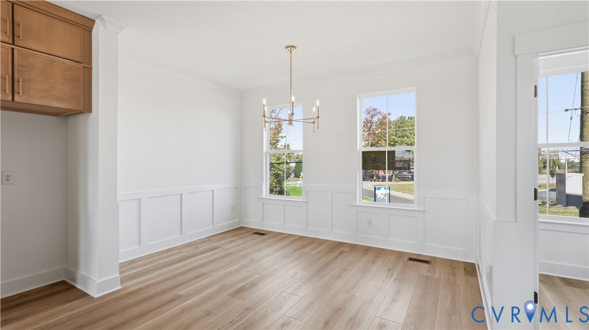 Bright interior featuring wood-finish flooring, white wall wainscoting, built-in cabinetry, dual-pane windows, and a metallic chandelier