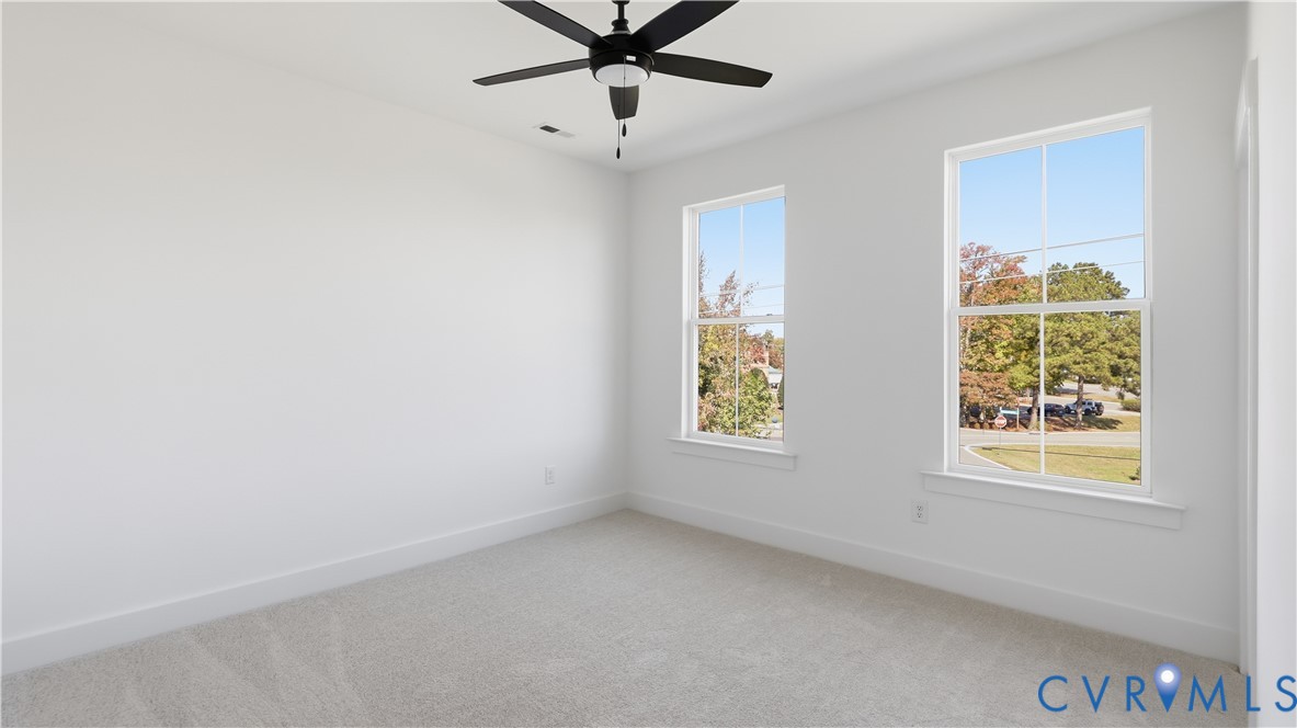 Neutral-toned carpeting, dual double-hung windows, and a matte black ceiling fan