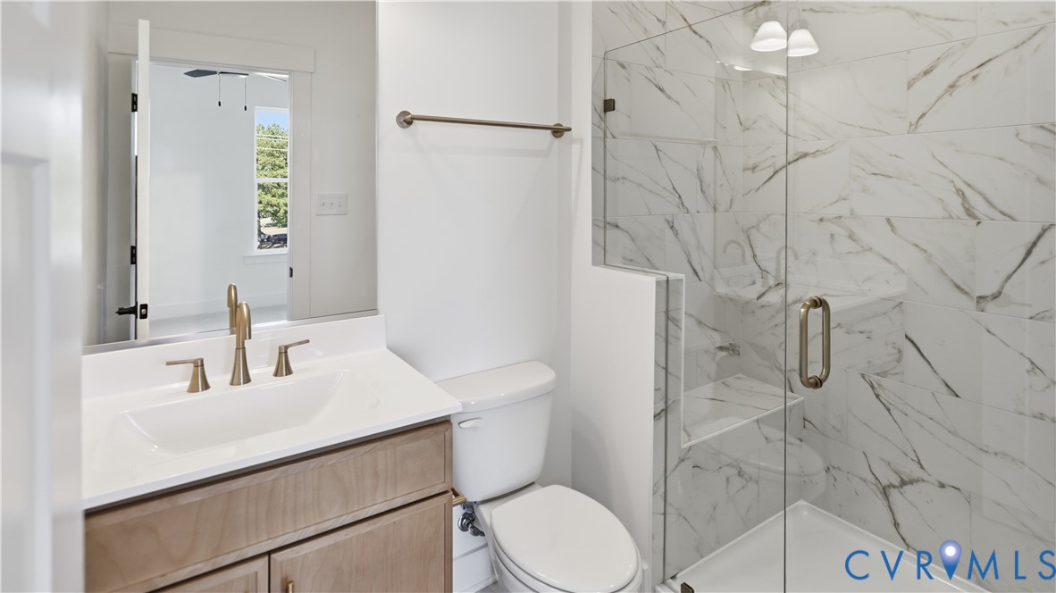 Bathroom featuring a vanity with an integrated sink and metal-finish faucet, a glass-enclosed shower with full-height stone-patterned tile surround, and a wall-mounted towel bar