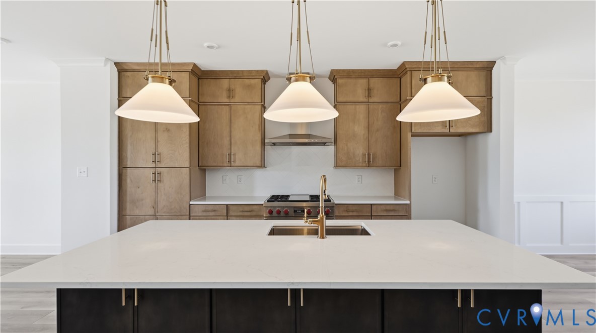 Kitchen featuring a large island with a quartz countertop, wood-finish cabinetry, stainless steel gas range, brass-tone hardware, and trio of pendant light fixtures