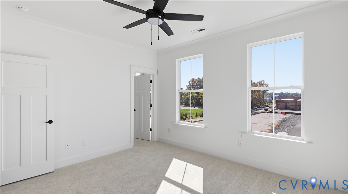 Neutral-toned room featuring neutral carpeting, double-hung windows, a multi-blade ceiling fan with integrated lighting, and solid-core paneled doors with matte black hardware