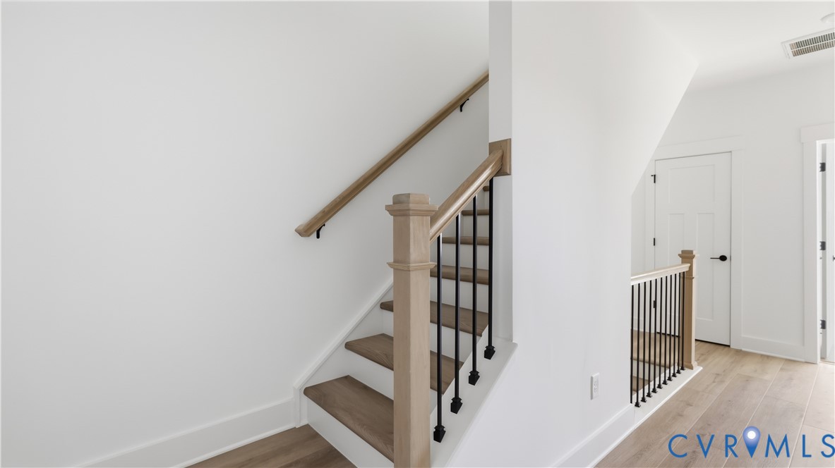 Staircase featuring wood-finish treads, a square newel post, a natural wood-finish handrail, and matte black metal balusters set against wood-finish flooring