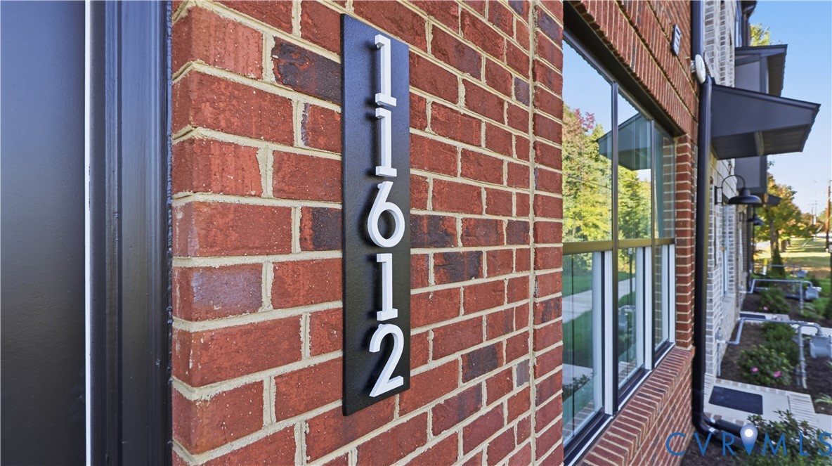 Red brick exterior featuring metal-framed windows, a matte black house number plaque with dimensional numbering, and dark-finished exterior light fixtures Red brick exterior featuring metal-framed windows, a matte black house number plaque with dimensional numbering, and dark-finished exterior light fixtures