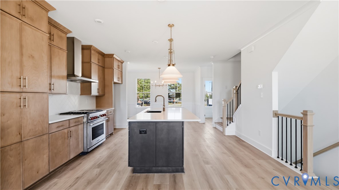 Kitchen featuring floor-to-ceiling wood cabinetry, stainless steel range with overhead vent hood, center island with stone-surface countertop, wood-finish flooring, and metal-spindle staircase railing