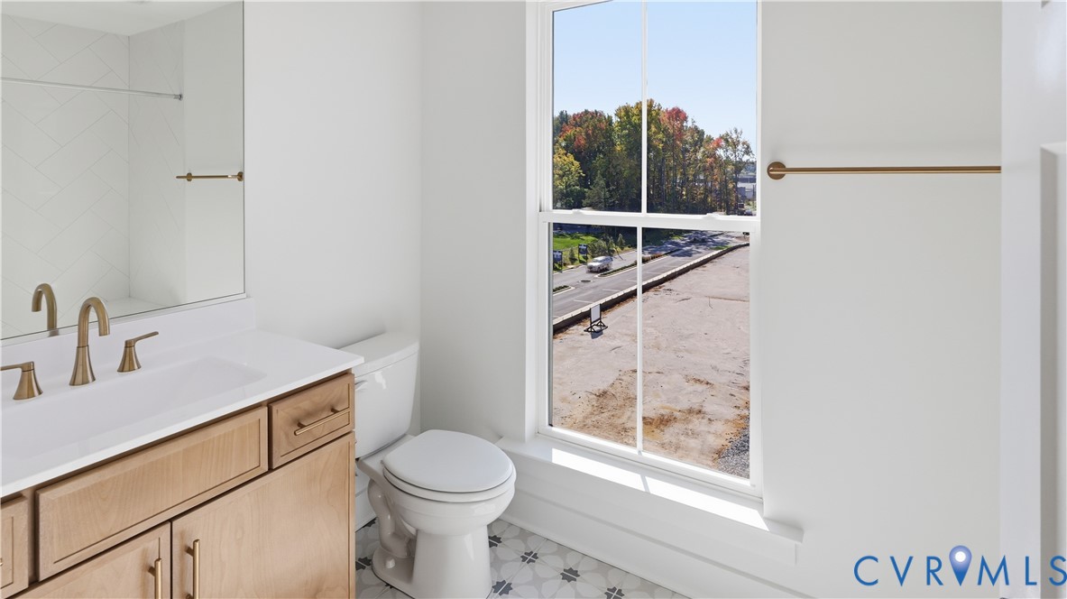 Light wood cabinetry with a solid surface countertop, brass-toned fixtures, a large window, and patterned tile flooring