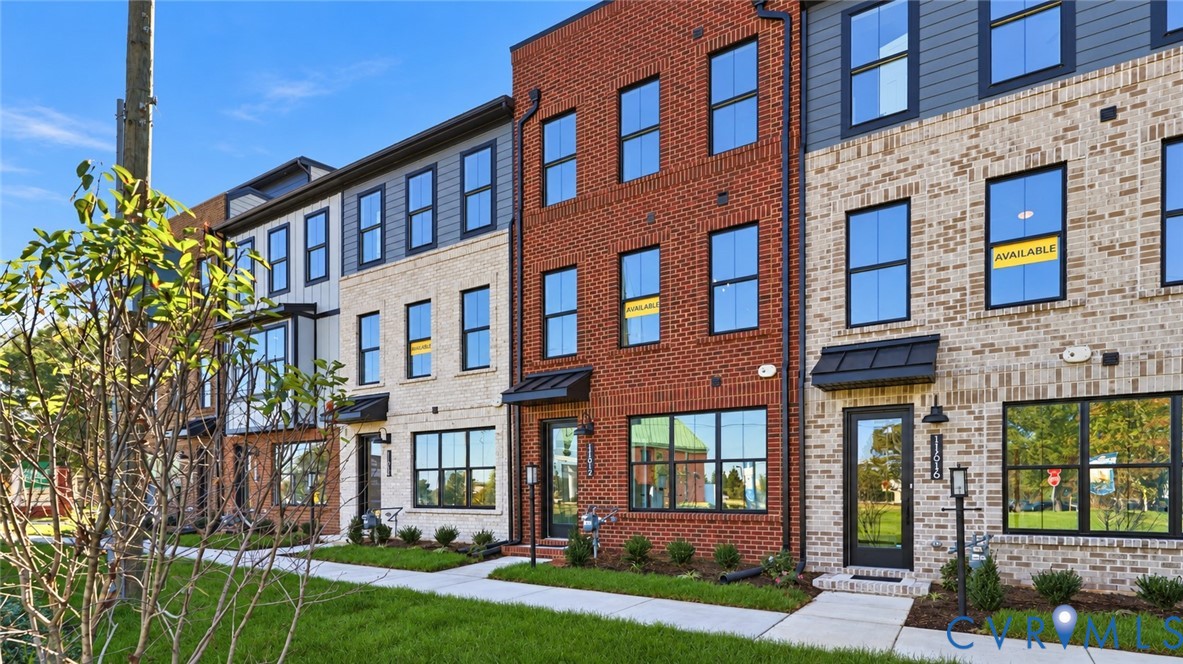 Multi-story brick and masonry exterior featuring large windows with black frames, metal door awnings, and architectural panel accents