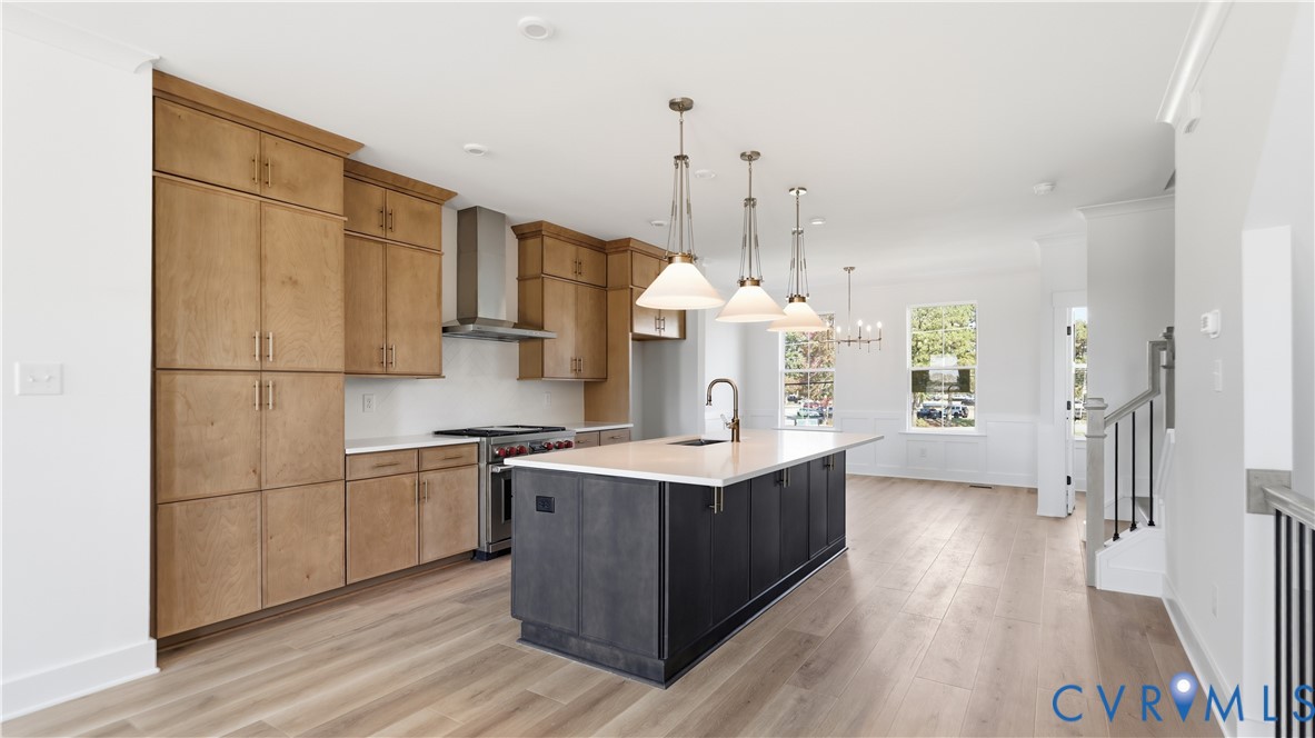 Kitchen featuring wood-finish cabinetry, a central island with a contrasting dark base and light countertop, stainless steel range with a professional-style hood, pendant lighting, and wood-finish flooring Kitchen featuring wood-finish cabinetry, a central island with a contrasting dark base and light countertop, stainless steel range with a professional-style hood, pendant lighting, and wood-finish flooring