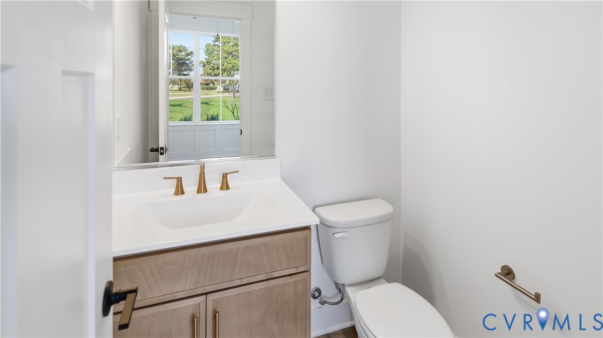 Vanity featuring a light wood-finish cabinet, white countertop with integrated sink, brass-tone hardware, and a frameless mirror Vanity featuring a light wood-finish cabinet, white countertop with integrated sink, brass-tone hardware, and a frameless mirror