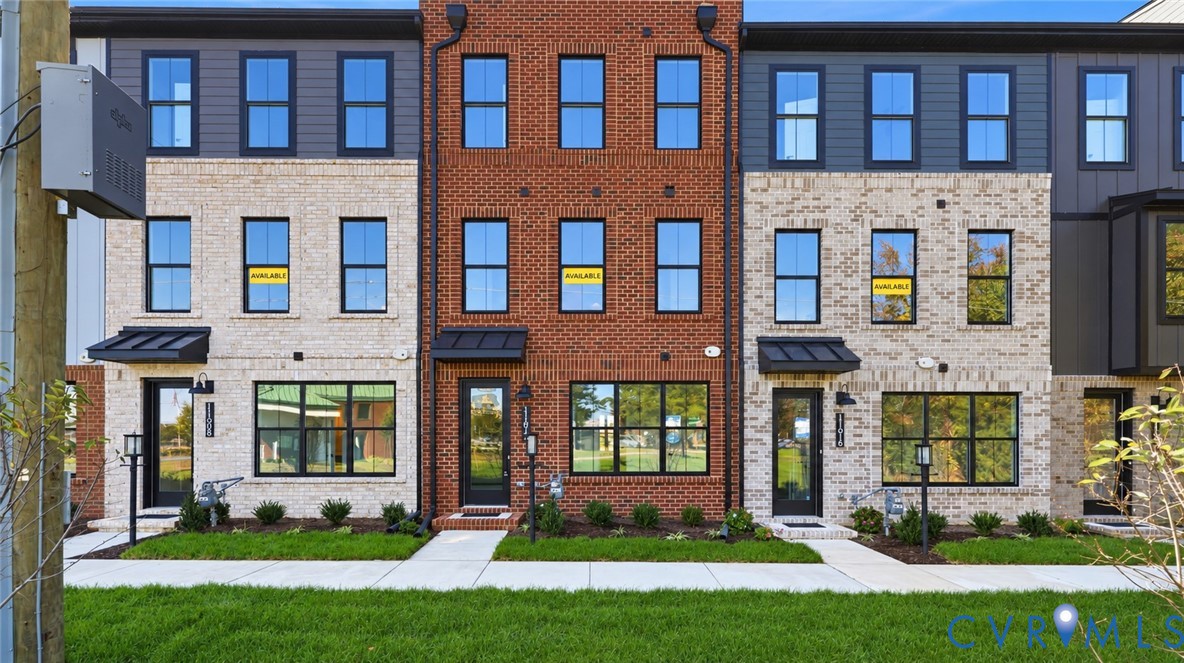 Modern three-story townhouse exterior featuring mixed-media brick and metal-panel siding, dark-framed multi-pane windows, and black metal door awnings