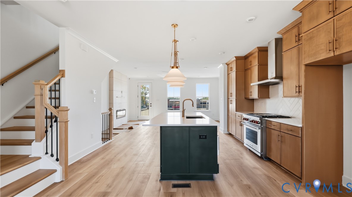 Kitchen featuring natural wood-finish cabinetry, a dark-toned center island with a stone countertop, stainless steel appliances, herringbone-patterned tile backsplash, and light wood-finish flooring