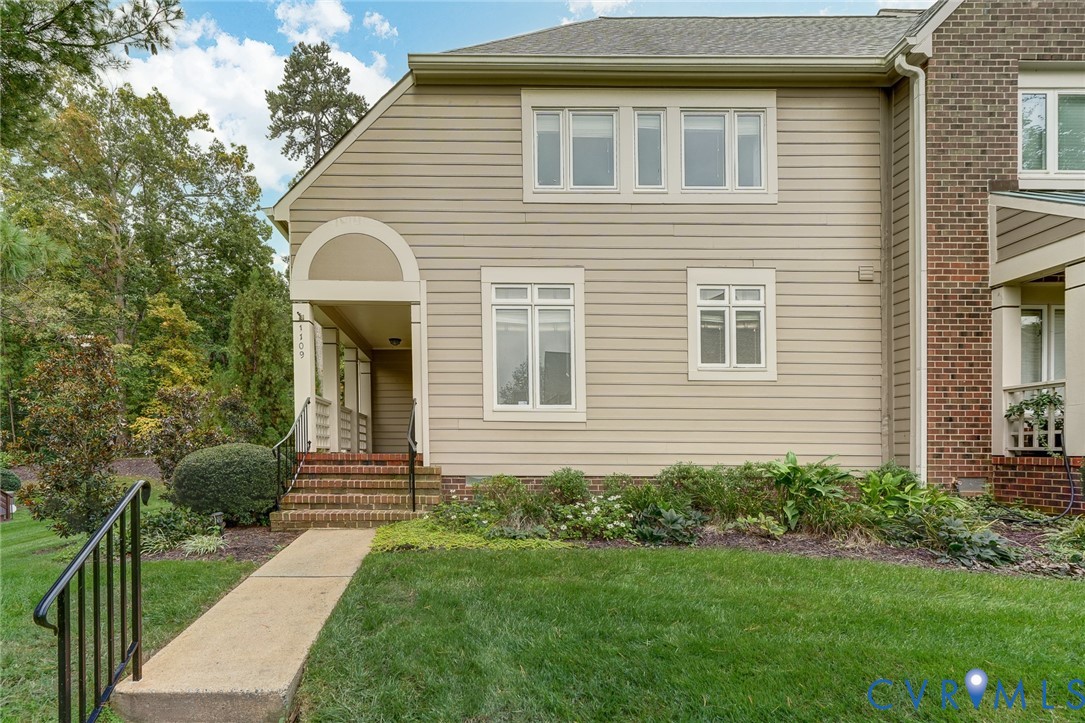 Exterior facade featuring horizontal siding and brick masonry accents, arched covered entryway, multi-pane windows, and a concrete walkway
