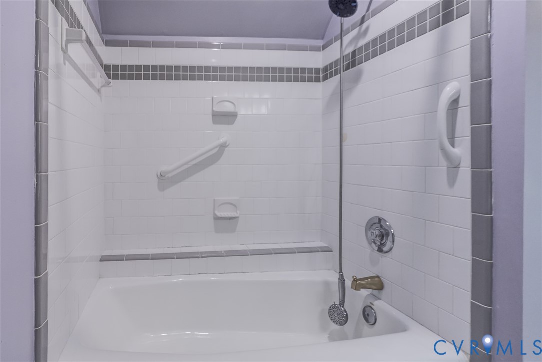 White subway tile shower surround with gray accent tiling, built-in soap dishes, wall-mounted hardware, and a tub with a handheld shower fixture