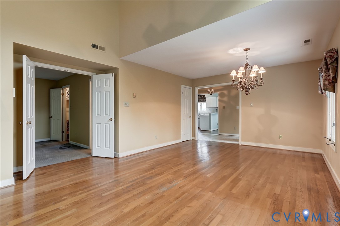Open-concept room featuring a vaulted ceiling, wood-finish flooring, and an ornate multi-arm chandelier