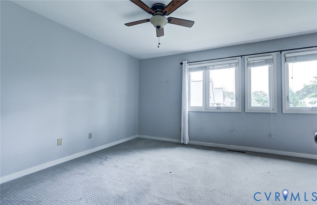Spacious room featuring neutral carpeting, triple-window configuration, and a ceiling fan with integrated lighting