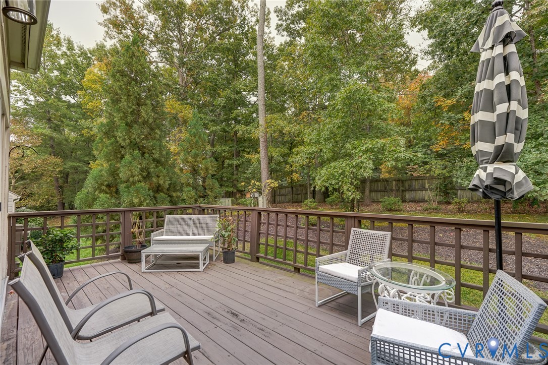 Elevated wood deck with perimeter latticed railings, overlooking a wooded lot with mature trees and a privacy fence