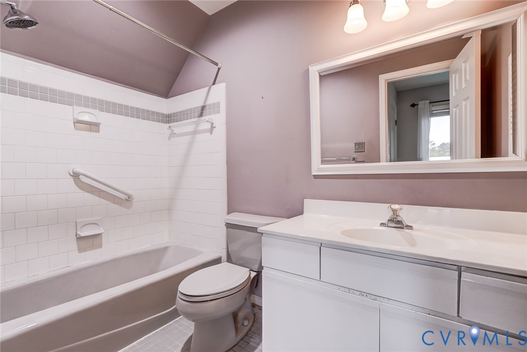 Bathroom featuring a white vanity with an integrated basin, framed wall mirror, three-light fixture, and a tub-shower combination with white wall tile