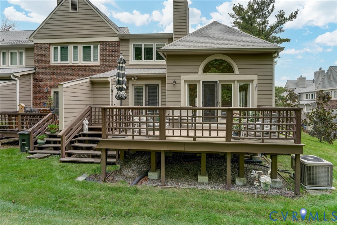 Exterior elevation featuring horizontal siding and brick masonry, an expansive raised wood deck with integrated railings, and arched window detailing