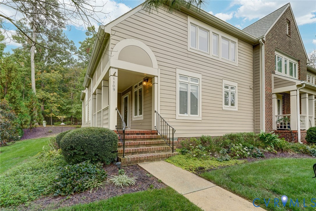 Multi-story exterior featuring a mix of brick and horizontal siding, covered front entryway, arched architectural detail, decorative metal railing, and concrete walkway Multi-story exterior featuring a mix of brick and horizontal siding, covered front entryway, arched architectural detail, decorative metal railing, and concrete walkway